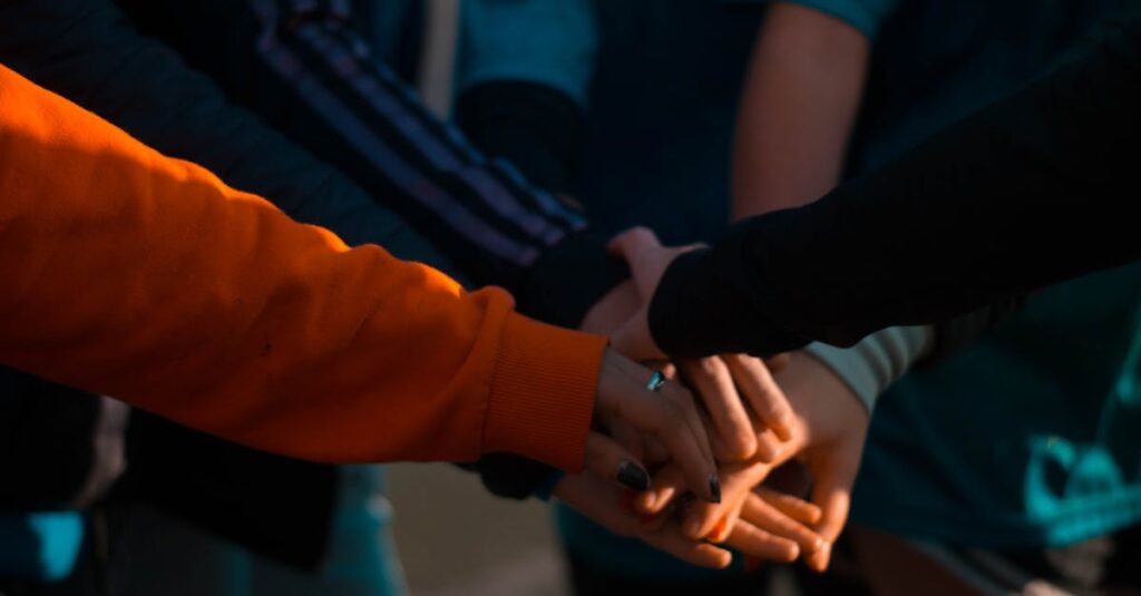 A close-up of diverse hands stacked together outdoors, symbolizing teamwork and unity.